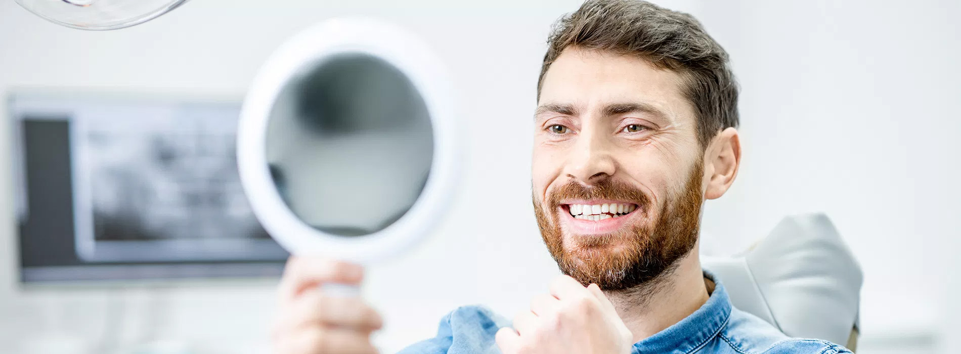 The image shows a man holding a large magnifying glass in front of his face while smiling at the camera.