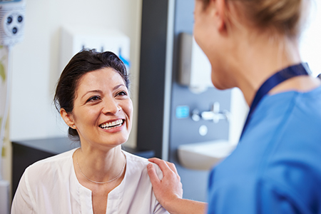 The image shows two individuals in a medical setting a woman wearing a white coat stands beside a man with a stethoscope around his neck, both smiling at each other.