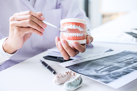 The image shows two photographs side by side on the left, a person s hand holding an open mouth model with a dental implant, and on the right, the same hand holding a cup of dental implants in front of a dental professional seated at a desk with various dental materials and equipment.