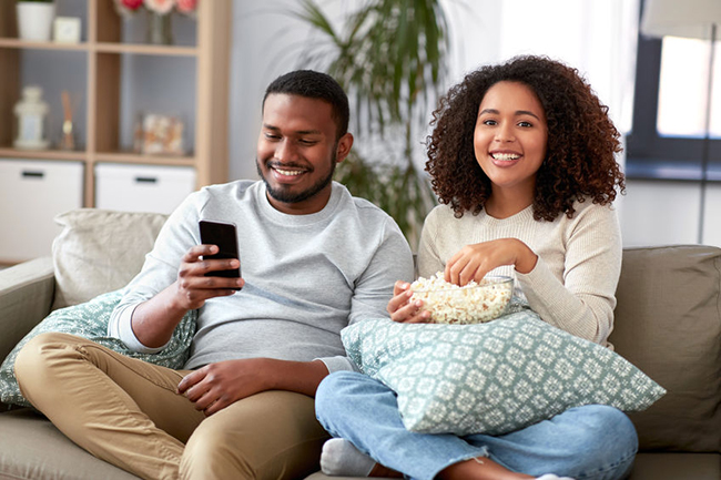 A man and woman sitting on a couch, sharing a moment together while enjoying popcorn.